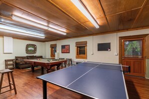 Una habitación con mesa de billar, mesa de tenis de mesa y estante para tacos de billar.