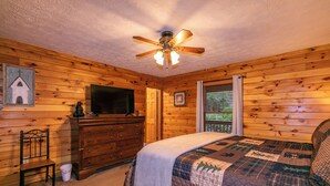 A wooden cabin bedroom with a bed, dresser, ceiling fan, and a television. - Heavens Hideaway (Ferguson)