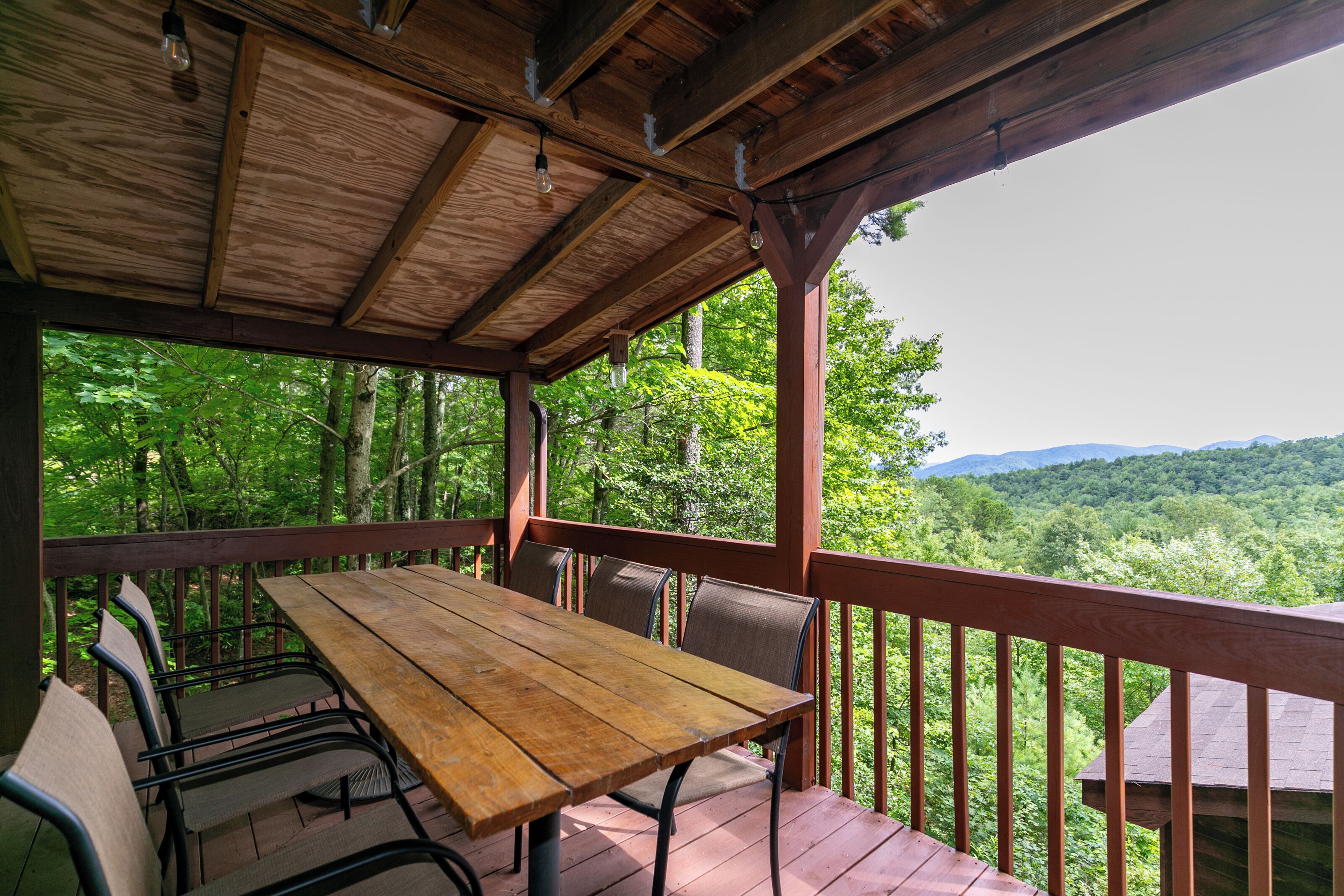 Eine Holzterrasse mit Tisch und Stühlen mit Blick auf eine bewaldete Landschaft.