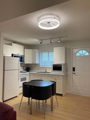 Une cuisine moderne avec des meubles blancs, une table à manger noire et un luminaire suspendu au plafond.