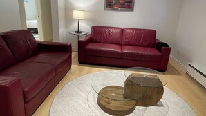 A living room with a red leather sofa, a glass coffee table, and a lamp. - Grate Location in Upper Lansdale North Vancouver (North Vancouver)