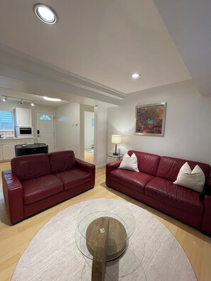 Ein modernes Wohnzimmer mit zwei roten Ledersofas, einem Glastisch und einer Küche im Hintergrund.