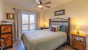A bedroom with a bed, a ceiling fan, a nightstand, a lamp, a dresser, and a window with curtains.