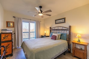 A bedroom with a bed, a ceiling fan, a nightstand, a lamp, a dresser, and a window with curtains.