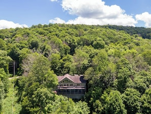 A house surrounded by dense forest, with a prominent balcony and a clear view of the sky.