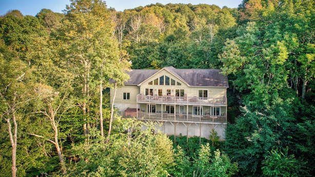 A two-story house with a balcony, surrounded by dense forest.