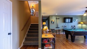 A home interior with a pool table, a game table with board games, a staircase, and a mirror.