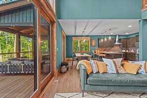 A cozy cabin interior with a dining area, kitchen, and a large window overlooking greenery.