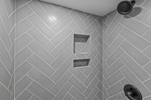 A shower area with a herringbone tile pattern, a showerhead, and a built-in shelf.