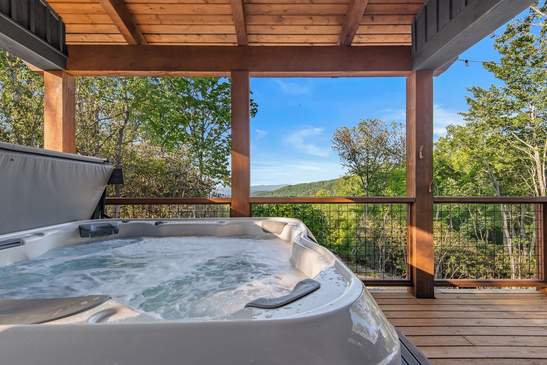 A hot tub on a wooden deck with a view of a forested landscape.
