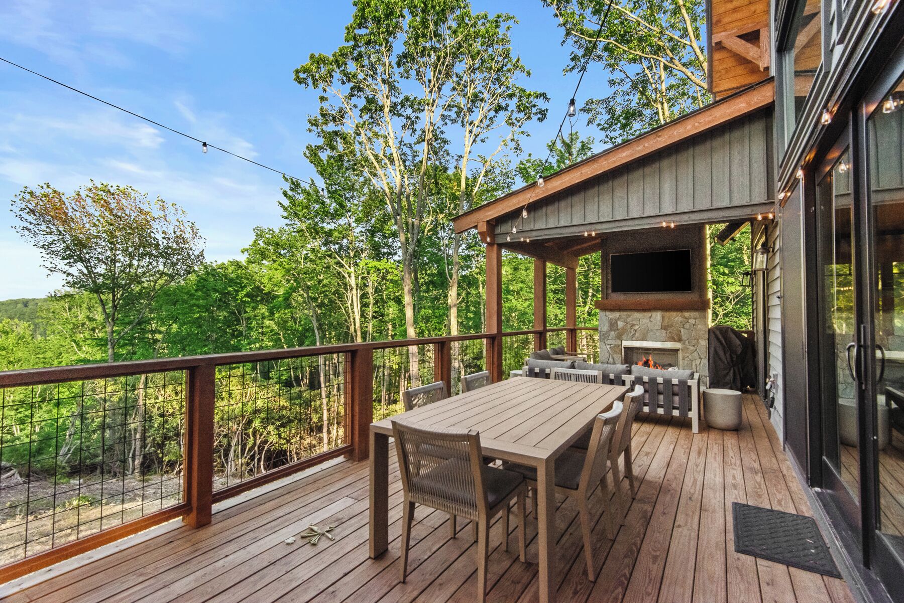 A wooden deck with outdoor furniture, a stone fireplace, and a TV mounted on the wall.