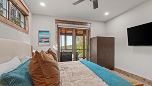 A bedroom with a bed, pillows, a wardrobe, a television, and a door leading to an outdoor area. - Bull & Bear at Eagles Nest (Banner Elk)