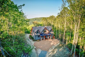 A two-story house with a wrap-around porch, surrounded by dense forest. - Bull & Bear at Eagles Nest (Banner Elk)