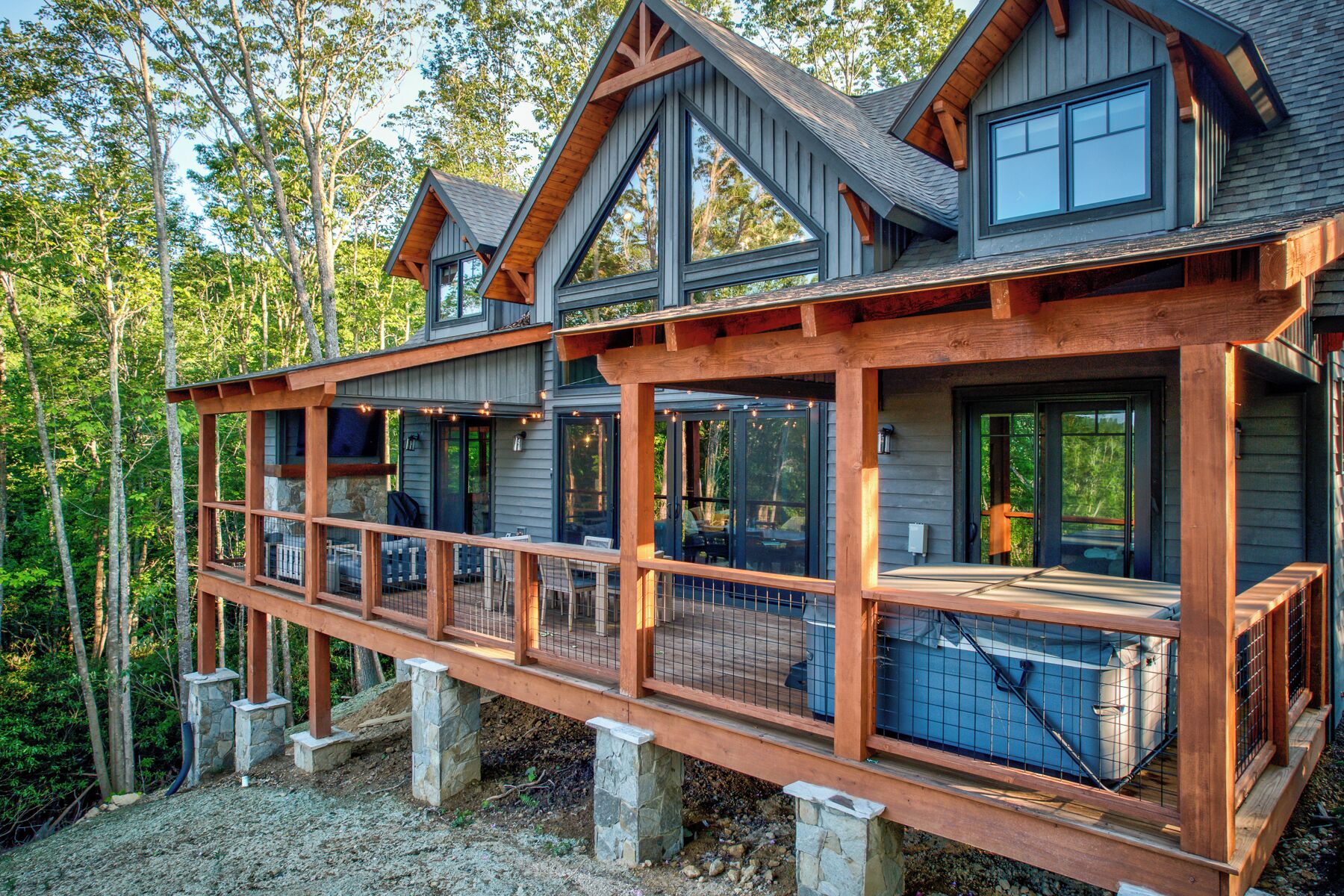 A two-story cabin with a deck, large windows, and a stone foundation.