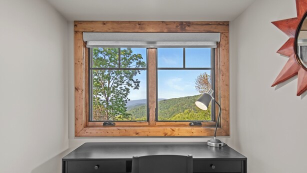 A room with a desk, a chair, a window with a view of trees and hills, and a lamp. - Bull & Bear at Eagles Nest (Banner Elk)
