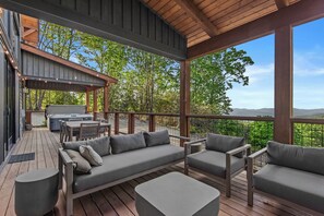 A covered outdoor deck with a wooden ceiling, a barbecue grill, and a seating area with sofas and chairs.