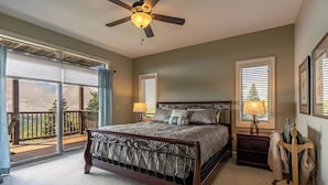 A bedroom with a large bed, a ceiling fan, a nightstand, a lamp, a dresser, and a balcony with a view. - Sugarjax at The Reserve (Banner Elk)