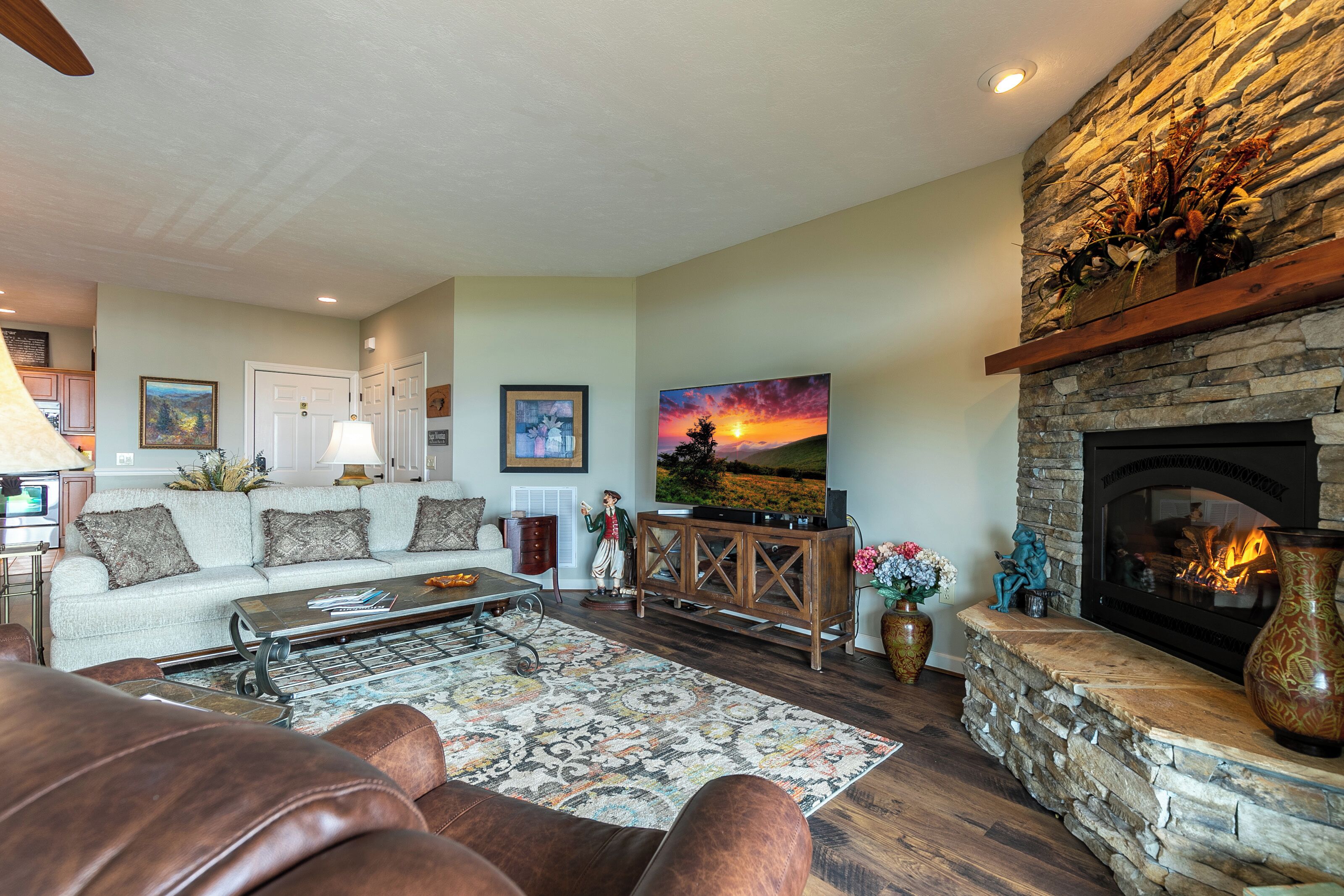 A living room with a stone fireplace, a sofa set, a coffee table, and a large painting of a sunset.