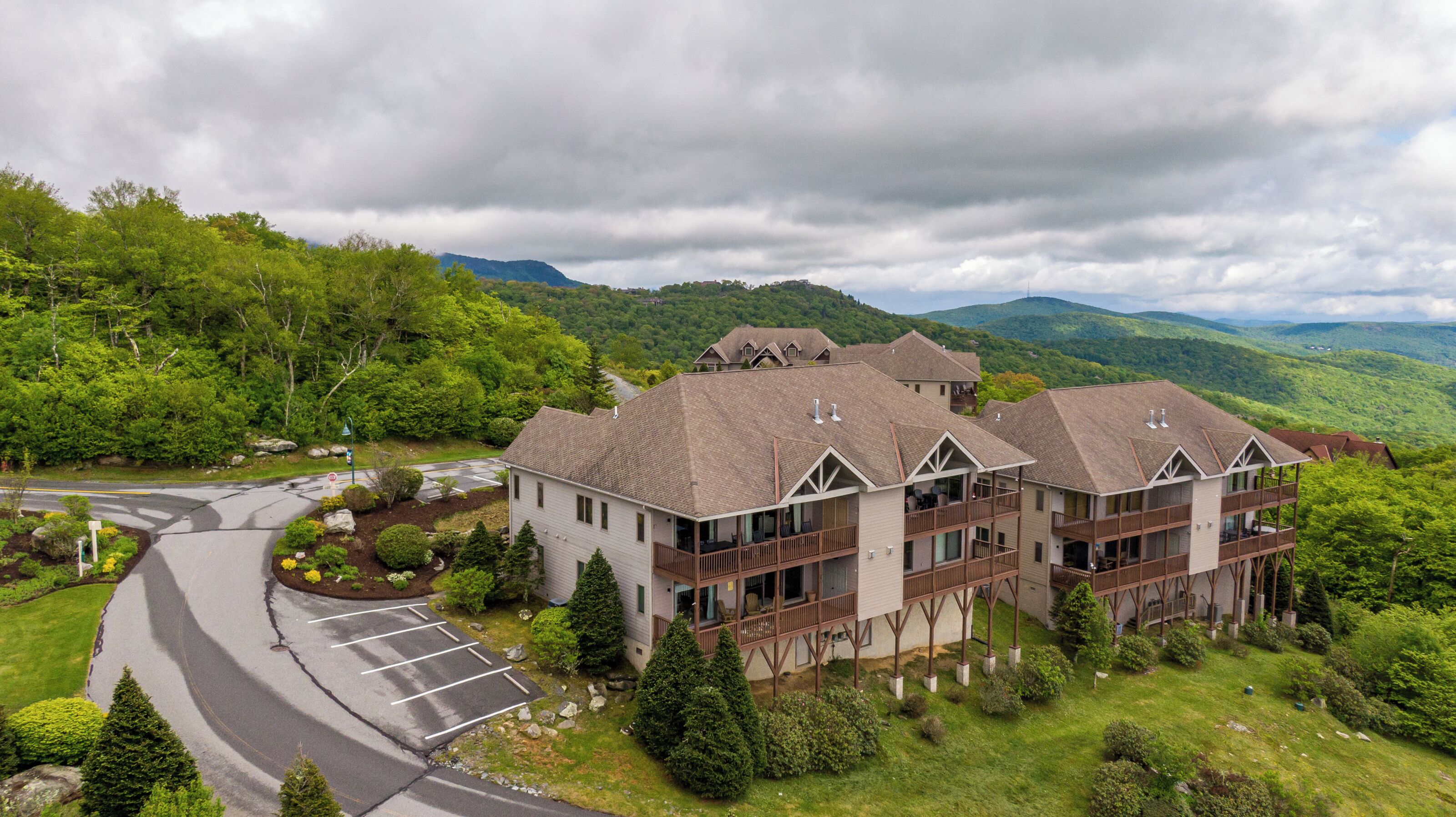 A multi-story building with balconies, surrounded by lush greenery and mountains.