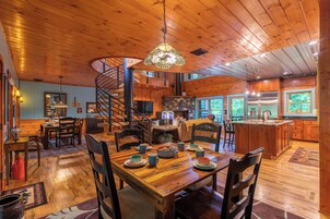 Interior espacioso de una cabaña de madera con comedor, cocina y una escalera en espiral.