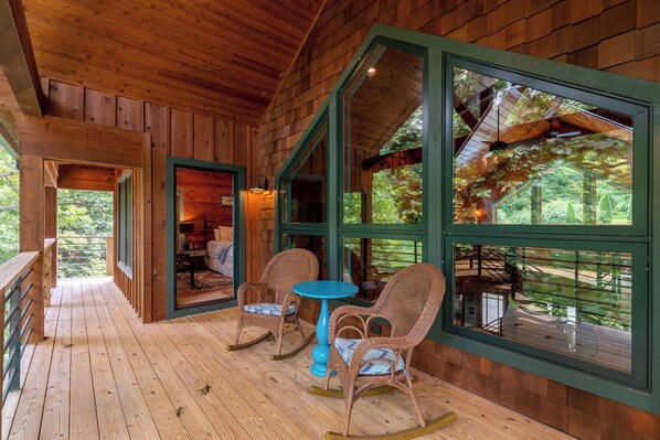A wooden cabin with a porch, rocking chairs, and a table.