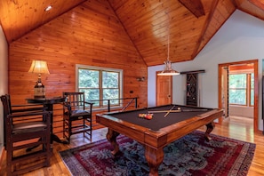 A wooden-paneled room with a pool table, chairs, and a lamp. - A River Mists Too (Sugar Grove)