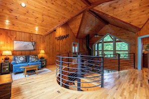 A wooden interior with a sofa, a coffee table, and a spiral staircase. - A River Mists Too (Sugar Grove)