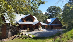 A lodge with a stone exterior, a covered porch, and a gravel driveway. - A River Mists Too (Sugar Grove)