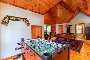 A spacious room with a foosball table, a pool table, wooden ceiling beams, and a banner reading 'APP STATE'.