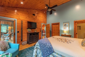 A log cabin interior with a bed, a TV, a ceiling fan, and a dining area with chairs.