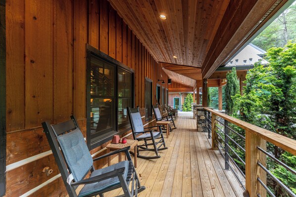 A wooden deck with rocking chairs and a railing overlooking a forested area.