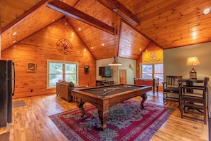 A wooden interior with a pool table, a television, and a flag.