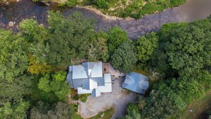 Vista aérea de una casa rodeada de un bosque denso, con un río que corre paralelo a la propiedad.