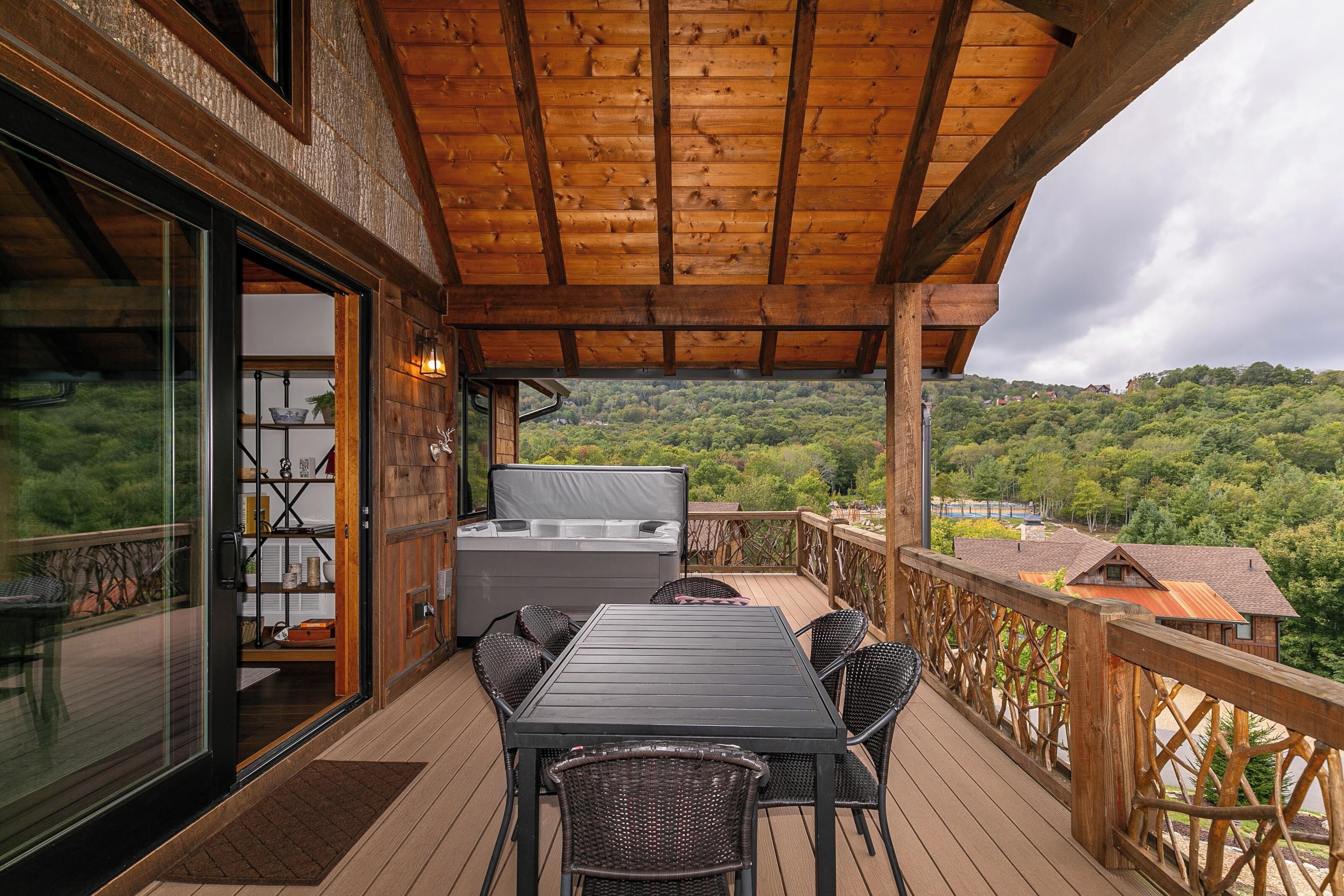 A wooden deck with a table and chairs, a hot tub, and a glass door leading to a room.