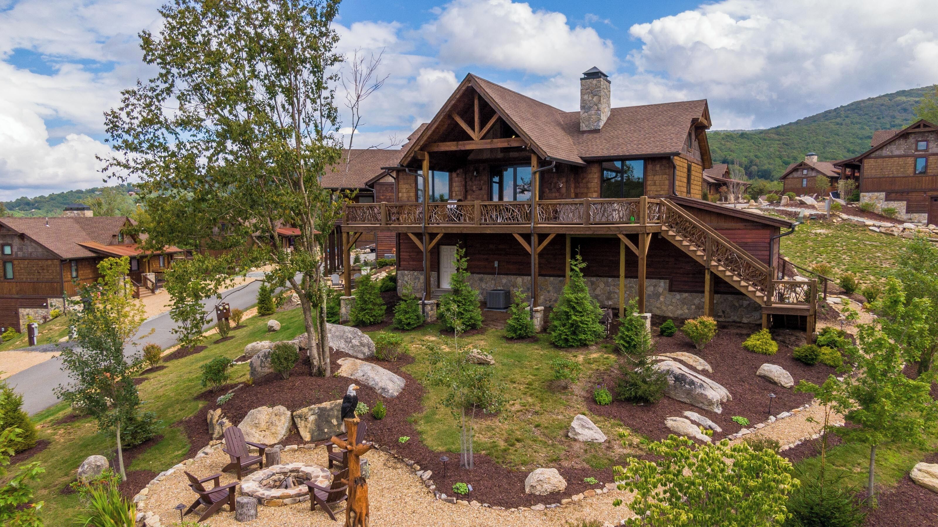 A lodge with a stone chimney, wooden deck, and a fire pit area.