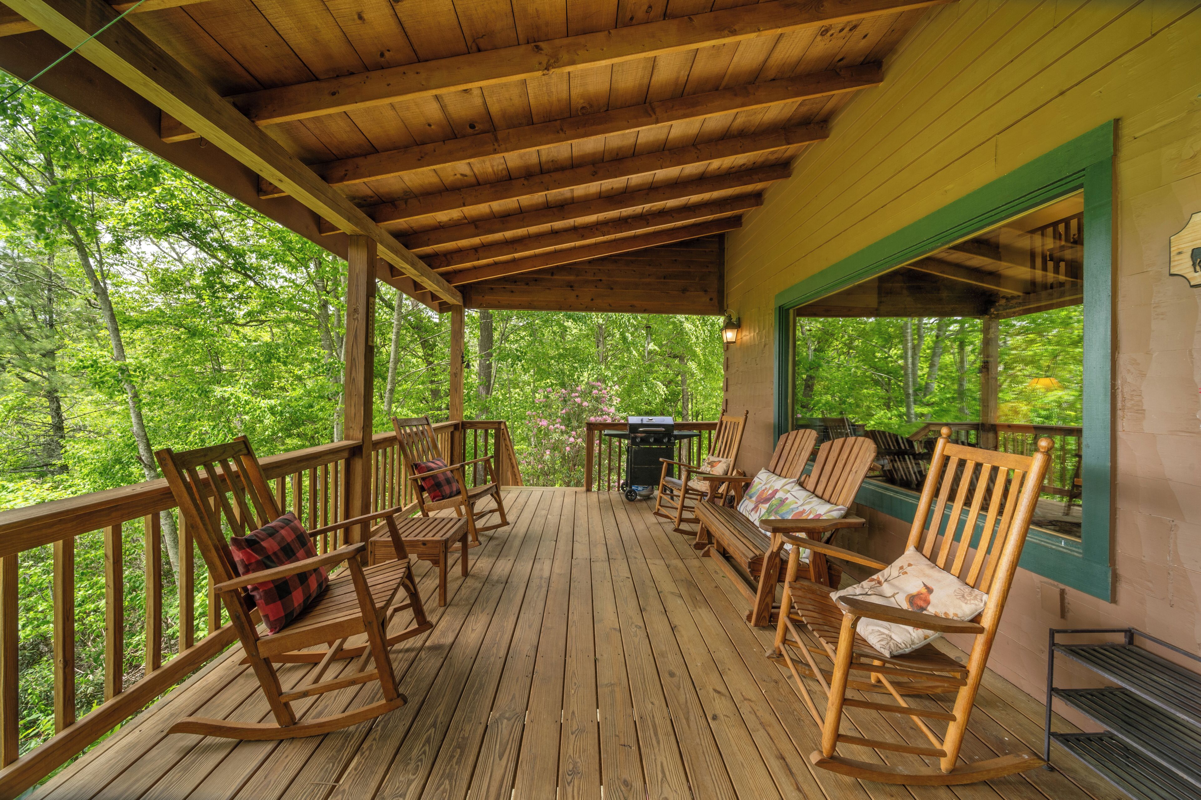 Une terrasse en bois, dotée de fauteuils à bascule et d’un barbecue, entourée d’arbres.