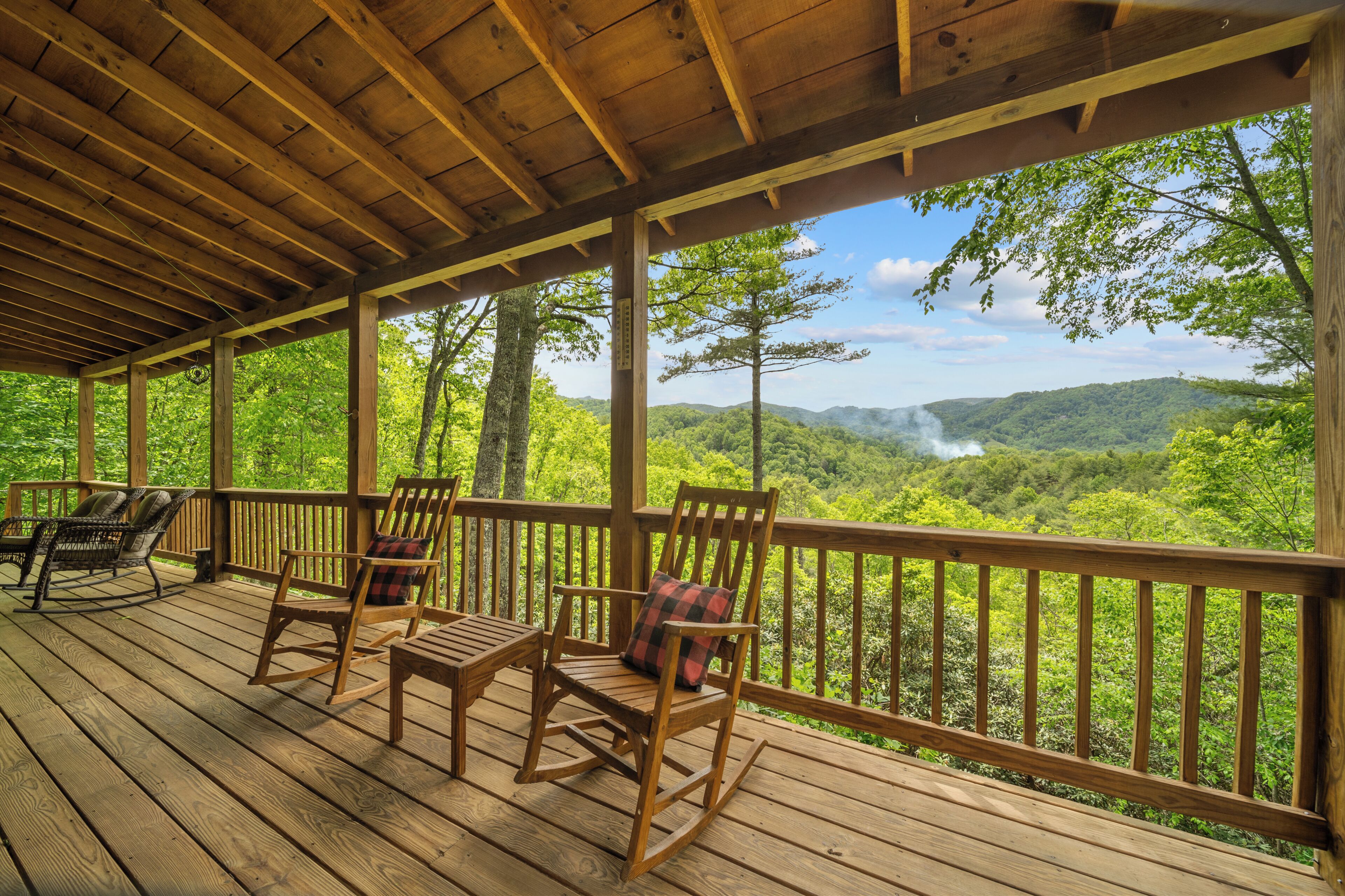A wooden deck with rocking chairs and a view of a forested landscape.