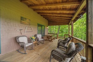 Eine überdachte Veranda mit Korbstühlen, einem Holztisch und einer an der Wand stehenden Leiter.