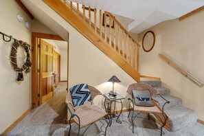 Eine Treppe mit Holzgeländern, ein kleiner Tisch mit Lampe, zwei Korbstühle mit Kissen und ein an der Wand befestigter Spiegel.
