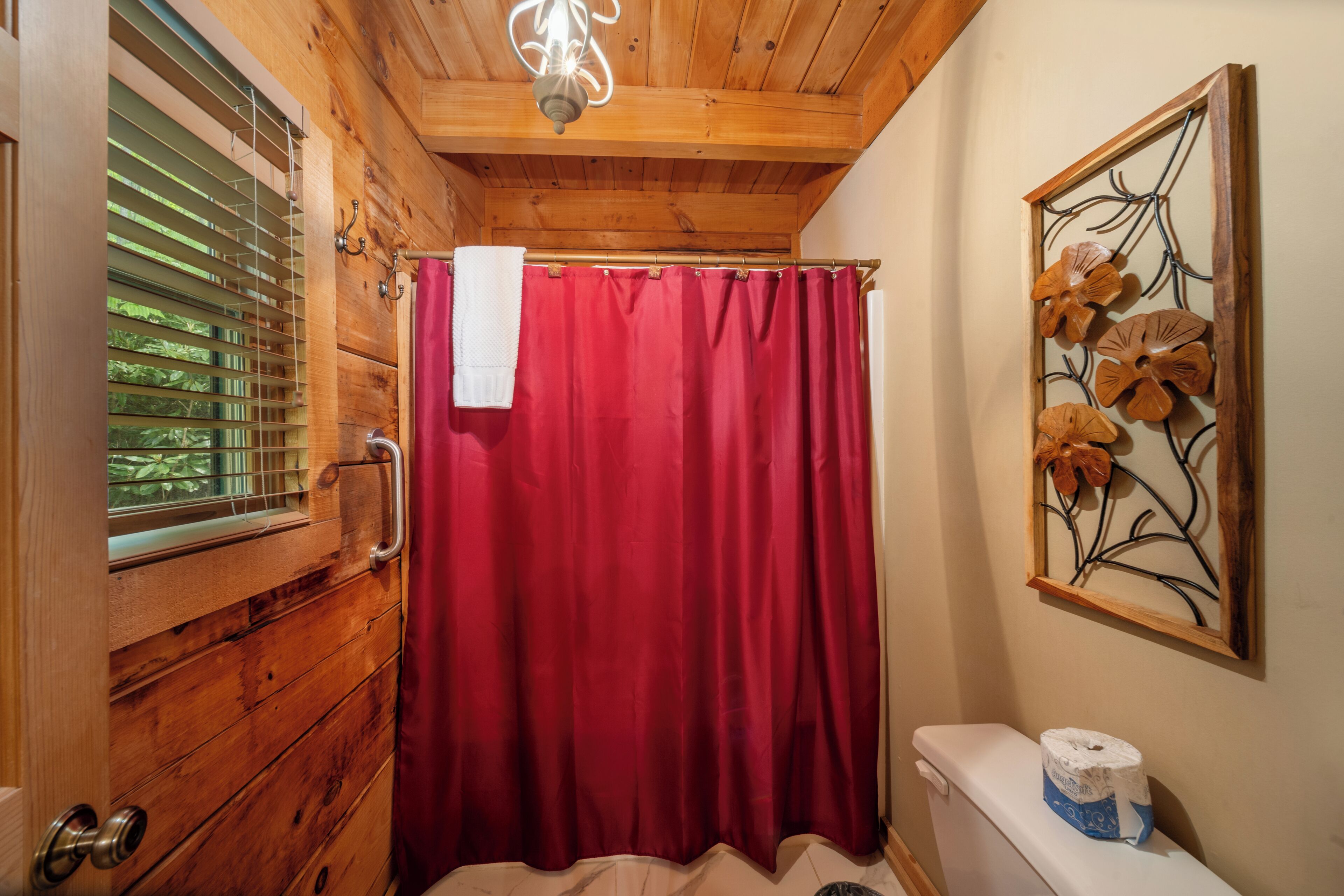 Un baño de madera con cortina de ducha roja, un inodoro y una ventana con persianas.
