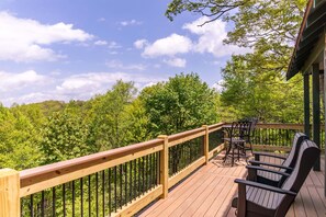 A wooden deck with a railing, outdoor furniture, and a view of a forested hillside. - Parkway Hideout (Boone)