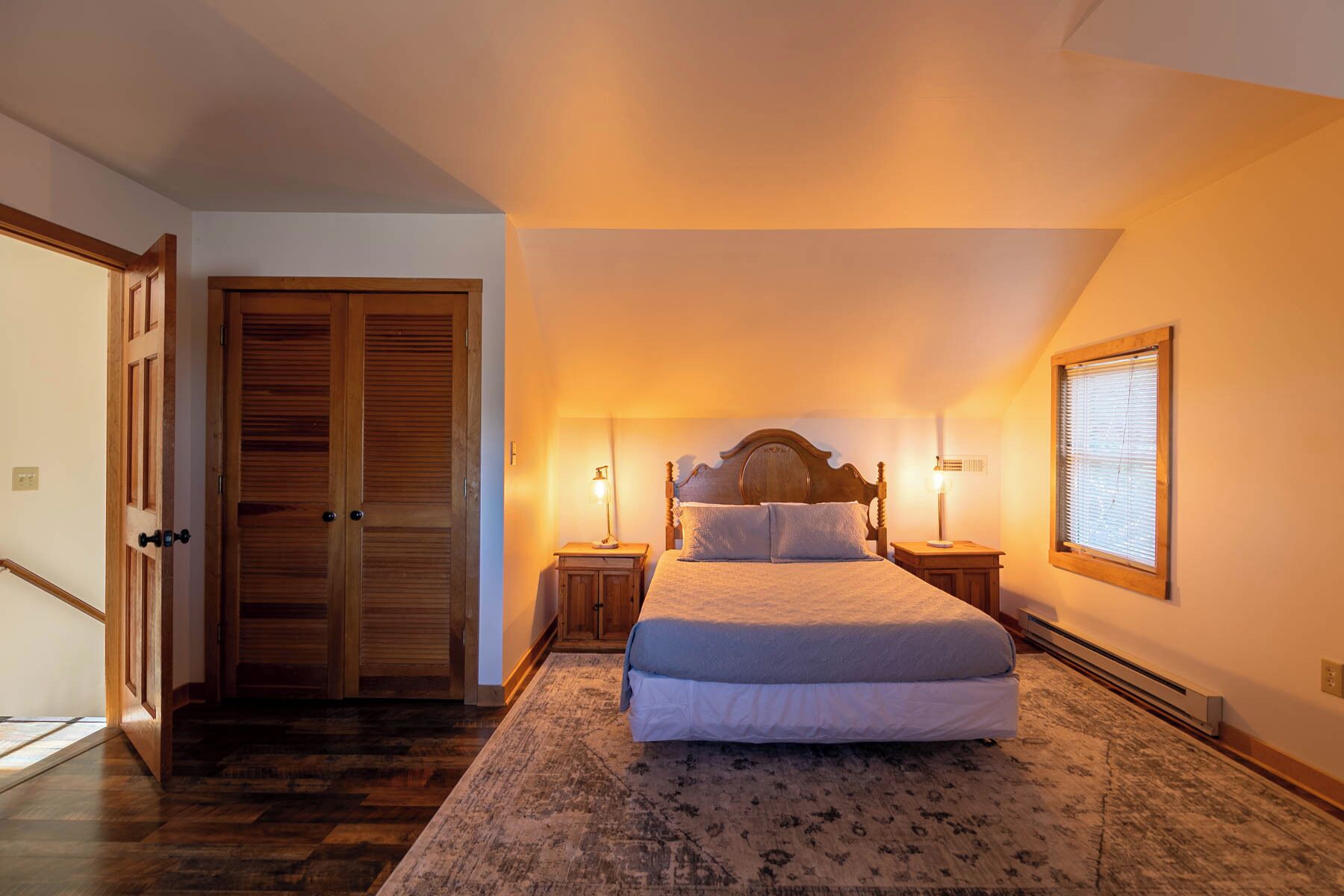 Une chambre avec un grand lit, une armoire en bois et une fenêtre avec des stores.