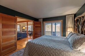 A bedroom with a large bed, wooden paneling, a view through a sliding door to a dining area, and a large window with a view of trees. - Parkway Hideout (Boone)