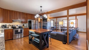 A spacious kitchen with wooden cabinets, a central island, and a stone fireplace. - Parkway Hideout (Boone)