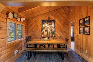 Un interior de madera con una mesa de comedor, sillas, una araña y un ventanal.