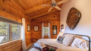 A log cabin bedroom with a bed, ceiling fan, windows, and wooden walls. - Angels Envy (Lenoir)