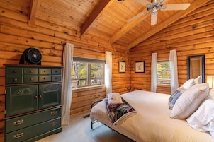 A wooden cabin bedroom with a bed, dresser, and windows.