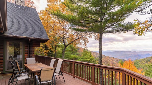 A wooden deck with a table and chairs, overlooking a forested landscape with autumn foliage. - Angels Envy (Lenoir)