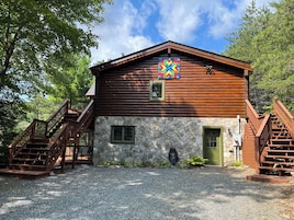 A wooden cabin with a stone facade, wooden stairs, and a colorful geometric sign.