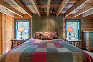 Ein Schlafzimmer einer Holzhütte mit einem großen Bett, zwei Fenstern und einer Steppdecke.